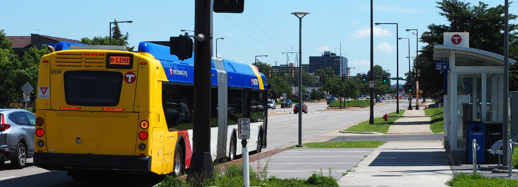 A D Line bus in blue and yellow Metro Transit livery stops at a station along American Boulevard.